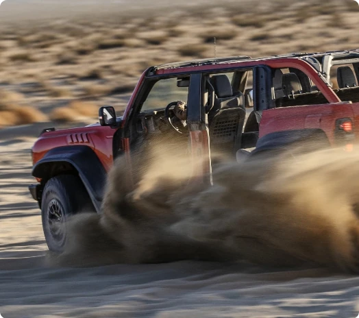 A Bronco Raptor kicks up sand while off-roading in the desert.
