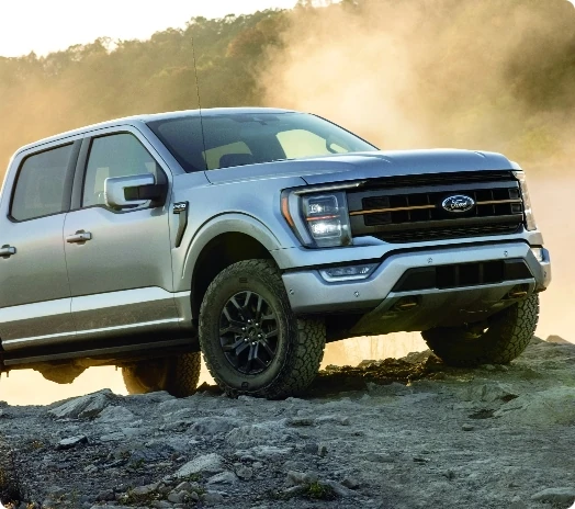 A Ford F-150 parked on rocky terrain with dust in the background.